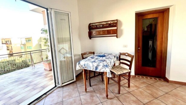 A balcony with a sliding glass door, a table with chairs, and a wooden door with a mirror. - Appartamento Mare Blu - Terracina (Terracina)