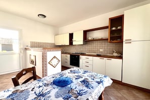A compact kitchen with white cabinets, a stove, and a dining area with a table set for two. - Appartamento Mare Blu - Terracina (Terracina)