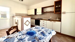 A compact kitchen with white cabinets, a tiled backsplash, and a dining table with a blue tablecloth. - Appartamento Mare Blu - Terracina (Terracina)