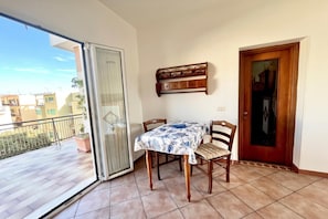 A balcony with a table and chairs, a sliding glass door, and a view of buildings. - Appartamento Mare Blu - Terracina (Terracina)