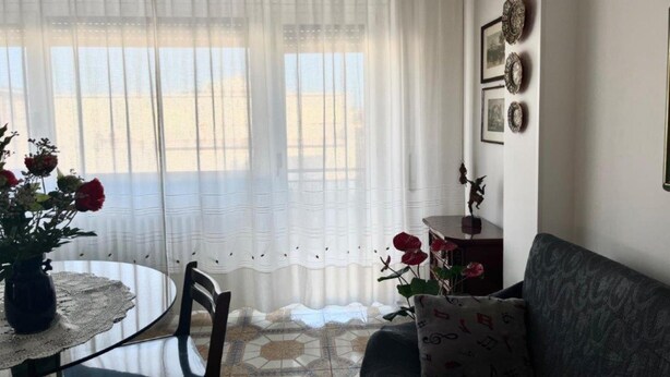 Ein Zimmer mit einem runden Tisch, einem Sofa und einem Fenster mit transparenten Vorhängen.