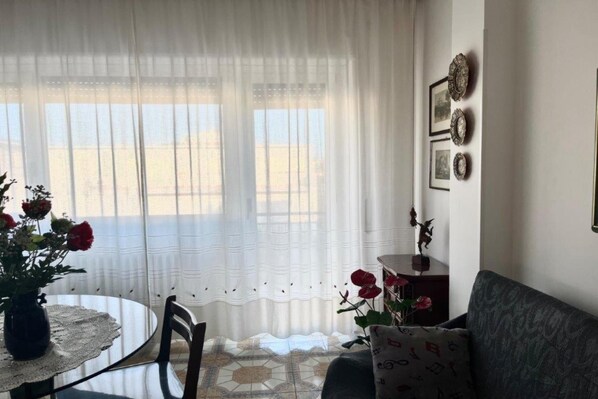 A room with a round table, a sofa, and a window with sheer curtains. - Appartamento Mare Blu - Terracina (Terracina)