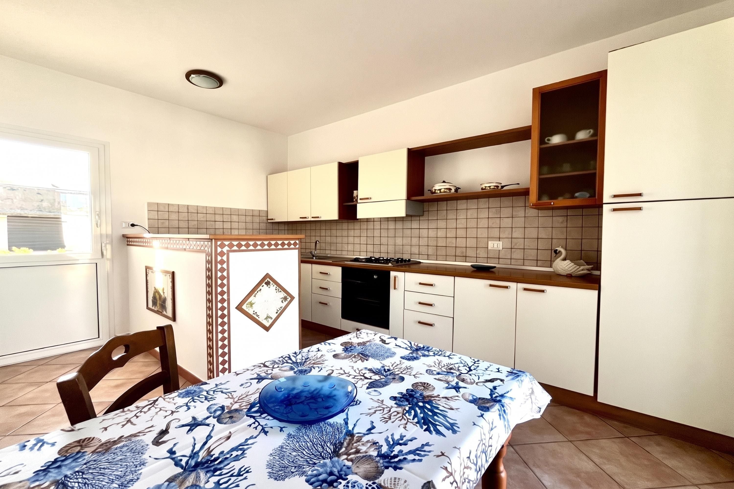 Cozinha compacta com armários brancos, fogão e área de jantar com mesa posta para dois.