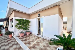 A modern building with a flat roof, a covered patio area with potted plants, and a sliding glass door. - Appartamento Mare Blu - Terracina (Terracina)