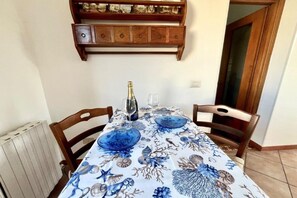 Une table à manger recouverte d’une nappe à motifs floraux, avec deux assiettes bleues, une bouteille de champagne et un verre.