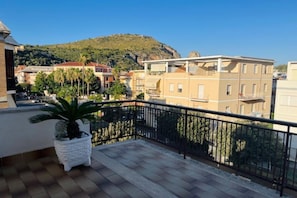 A balcony with a potted palm tree, a tiled floor, and a view of buildings and a hill in the background. - Appartamento Mare Blu - Terracina (Terracina)
