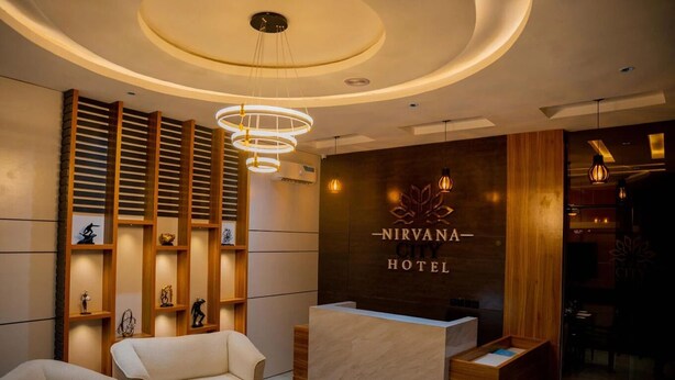 A reception area with a wooden reception desk, a sofa, and a wall with shelves displaying trophies and figurines. - Nirvana City Hotel (Benin City)