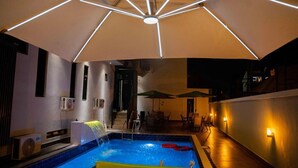 A rooftop pool area with a large umbrella, outdoor seating, and a staircase leading to an upper level. - Nirvana City Hotel (Benin City)