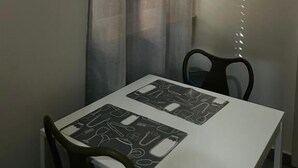 A dining area with a table and chairs, a window with sheer curtains, and a wall-mounted artwork. - Residence Cicerone (Agrigento)