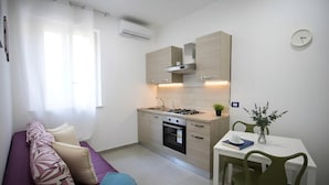 A compact kitchen with a stove, oven, and cabinets, a dining table with chairs, and a sofa with cushions. - Residence Cicerone (Agrigento)