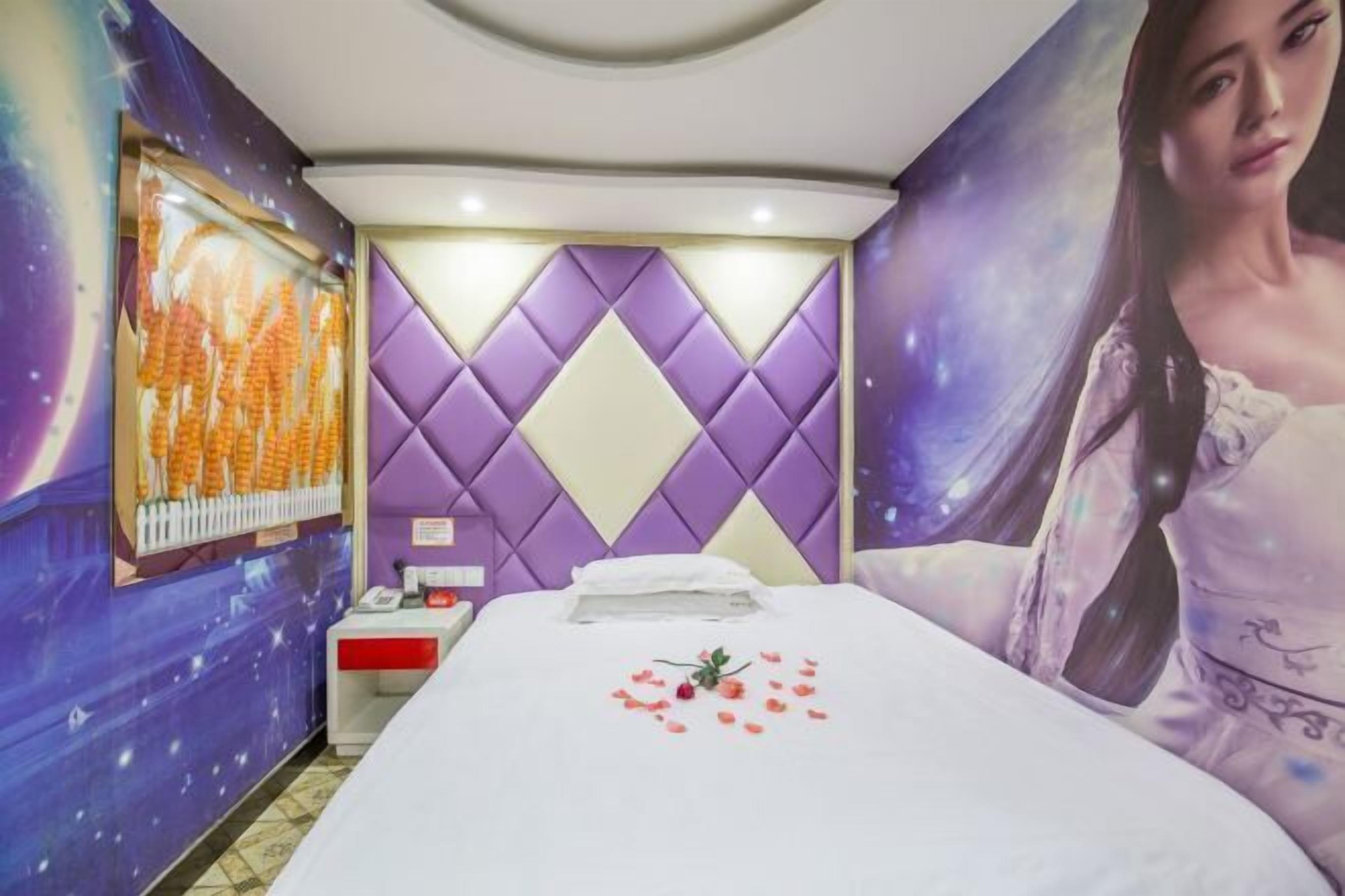 Een hotelkamer met een bed, nachtkastje, een televisie aan de muur en een groot poster.