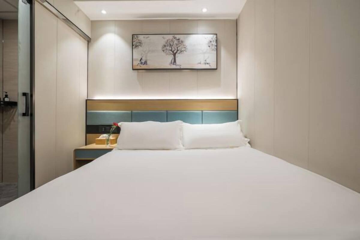 A hotel room with a bed, a nightstand, a painting on the wall, and a door to the left.