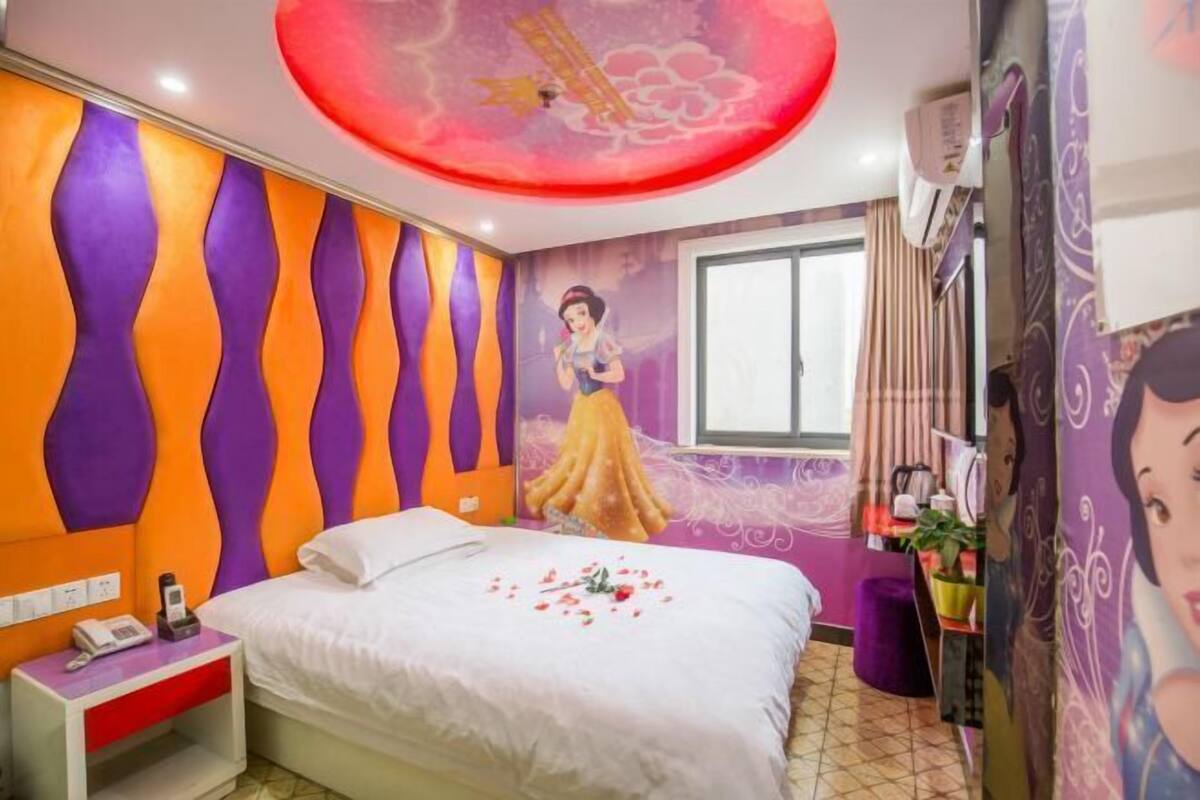 A bedroom with a bed, a nightstand, a wall mural, a window, and a curtain.