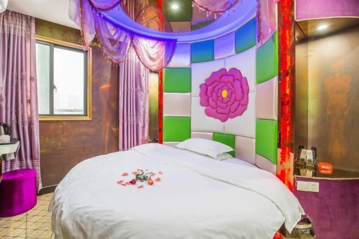 A hotel room with a bed, a window, a vanity, and a colorful wall design.