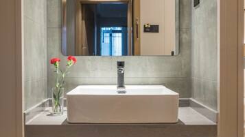 A bathroom with a rectangular sink, a mirror, and a vase with red flowers.
