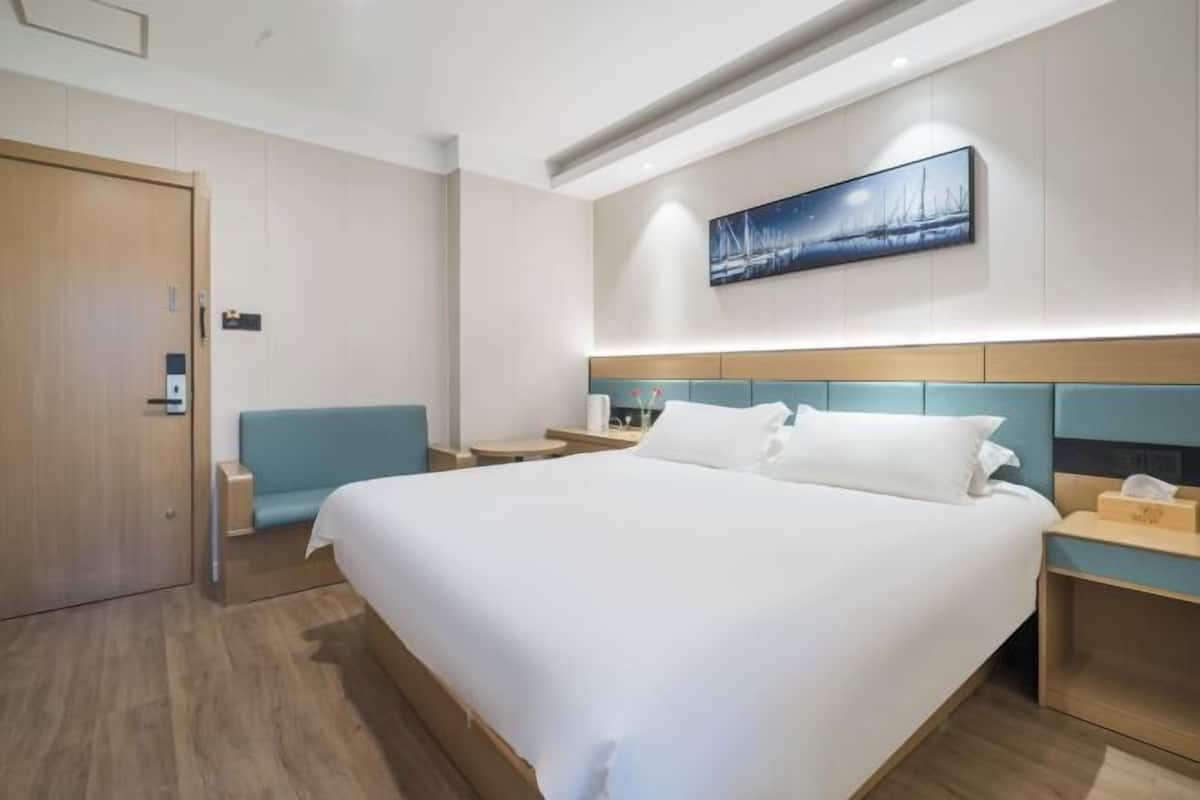A modern hotel room with a large bed, a seating area, a painting on the wall, and a wooden door.