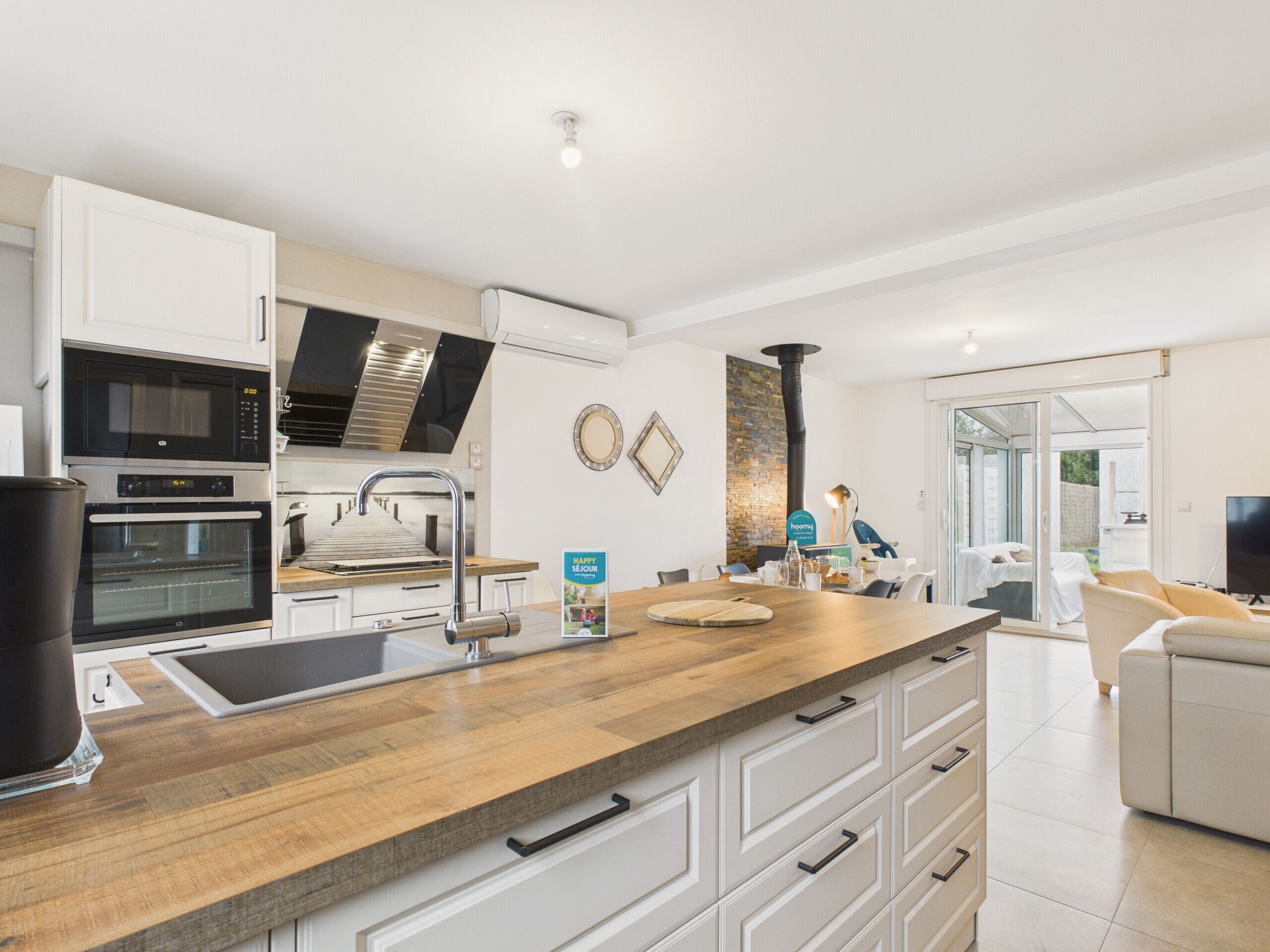 A modern kitchen with built-in appliances, a wooden countertop, and a dining area with a sofa and TV.