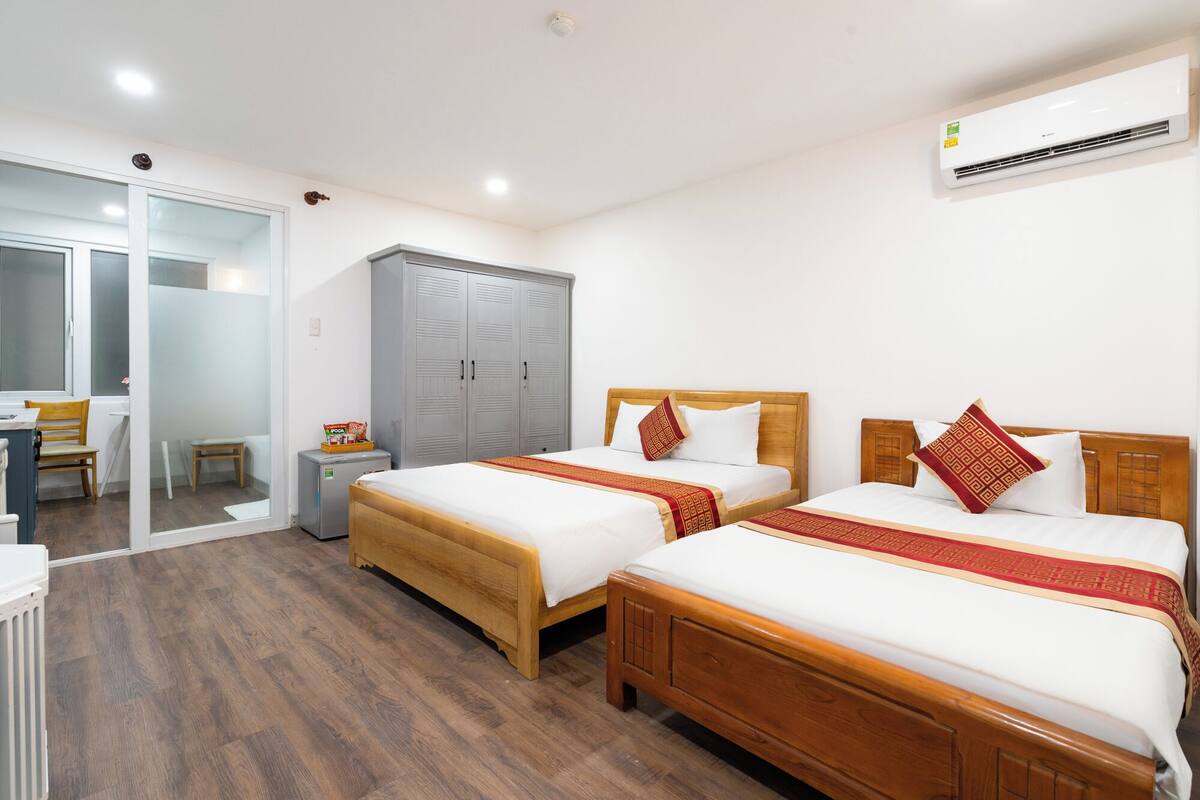 Habitación de hotel con dos camas de madera, un armario, un escritorio y un equipo de aire acondicionado.