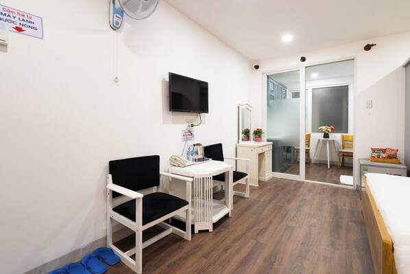 A hotel room with a bed, a desk with a chair, a TV, a mirror, a small table with chairs, and a sliding glass door leading to a balcony. - HELEN AIRPORT HOTEL (Ho Chi Minh City)