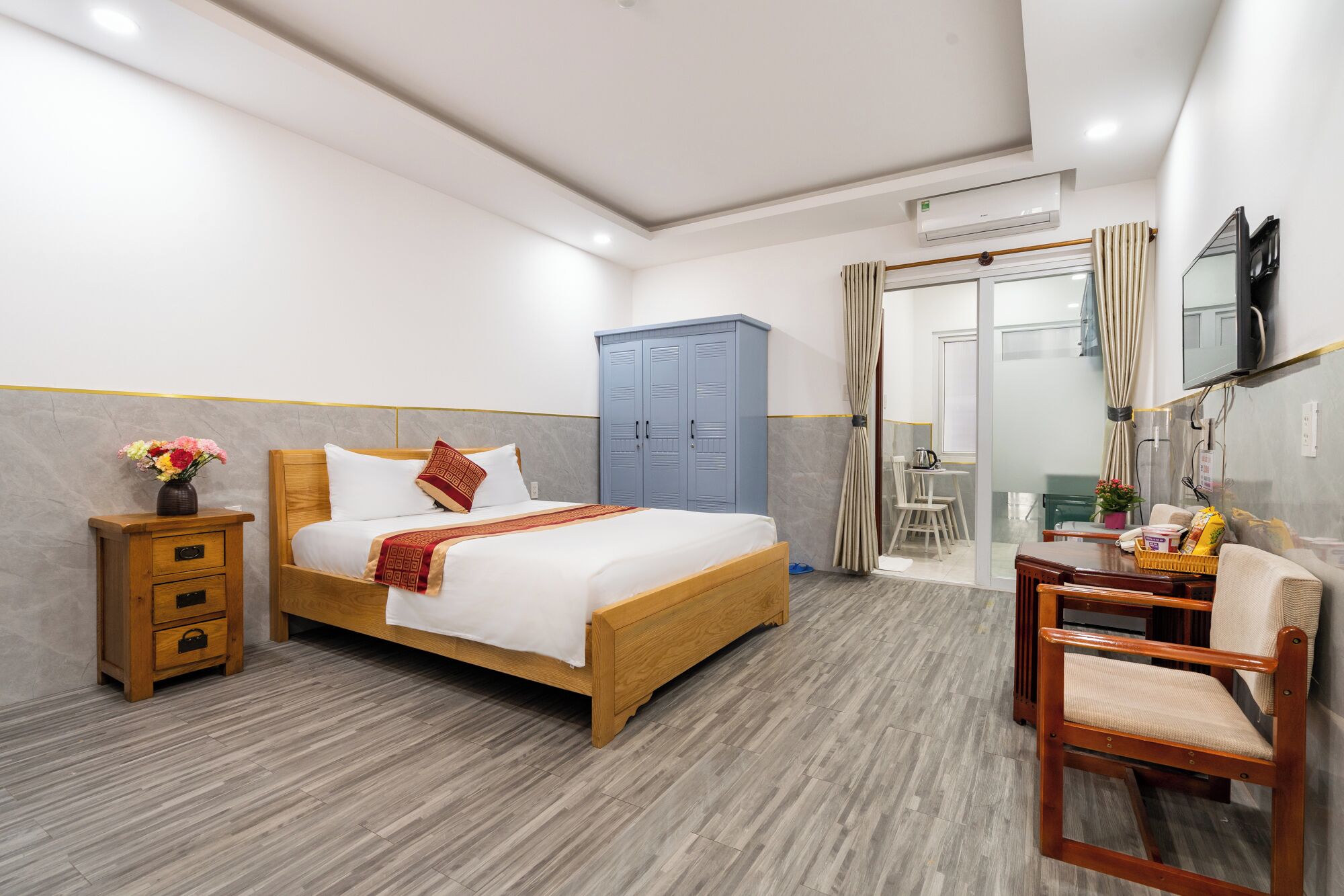 Une chambre d’hôtel avec un lit en bois, un bureau avec une chaise, une armoire et un téléviseur fixé au mur.