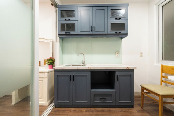 A compact kitchen with grey cabinets, a white countertop, and a wooden chair. - HELEN AIRPORT HOTEL (Ho Chi Minh City)