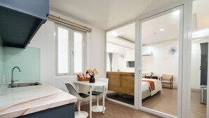 Ein modernes Hotelzimmer mit Küchenzeile, einem Esstisch mit Stühlen, einem Bett mit Holz-Kopfteil und einer Schiebetür zu einem Balkon.