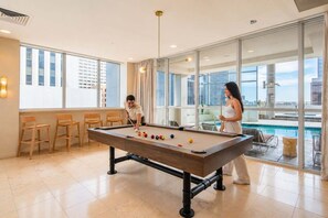 A pool table in a room with large windows, a view of a building, and a pool outside. - Stylish ASU Stay Pool Gym Balcony Parking WD (Phoenix)