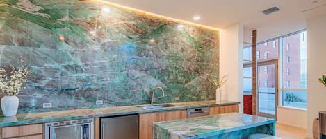 A modern kitchen with a marble backsplash, stainless steel appliances, and a bar area with stools.