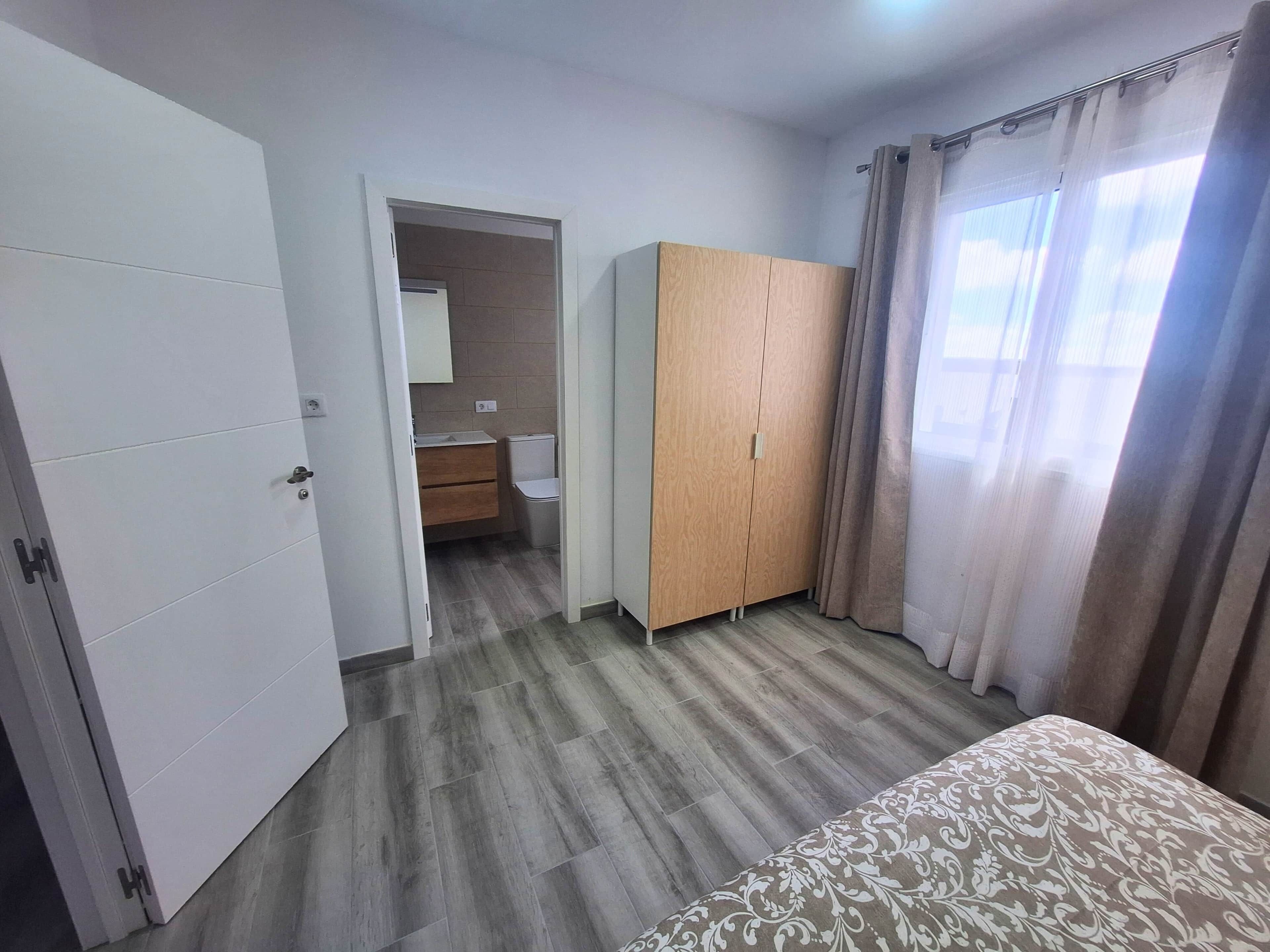 Une chambre à coucher avec un lit, une armoire et une salle de bain visible à travers une porte ouverte.