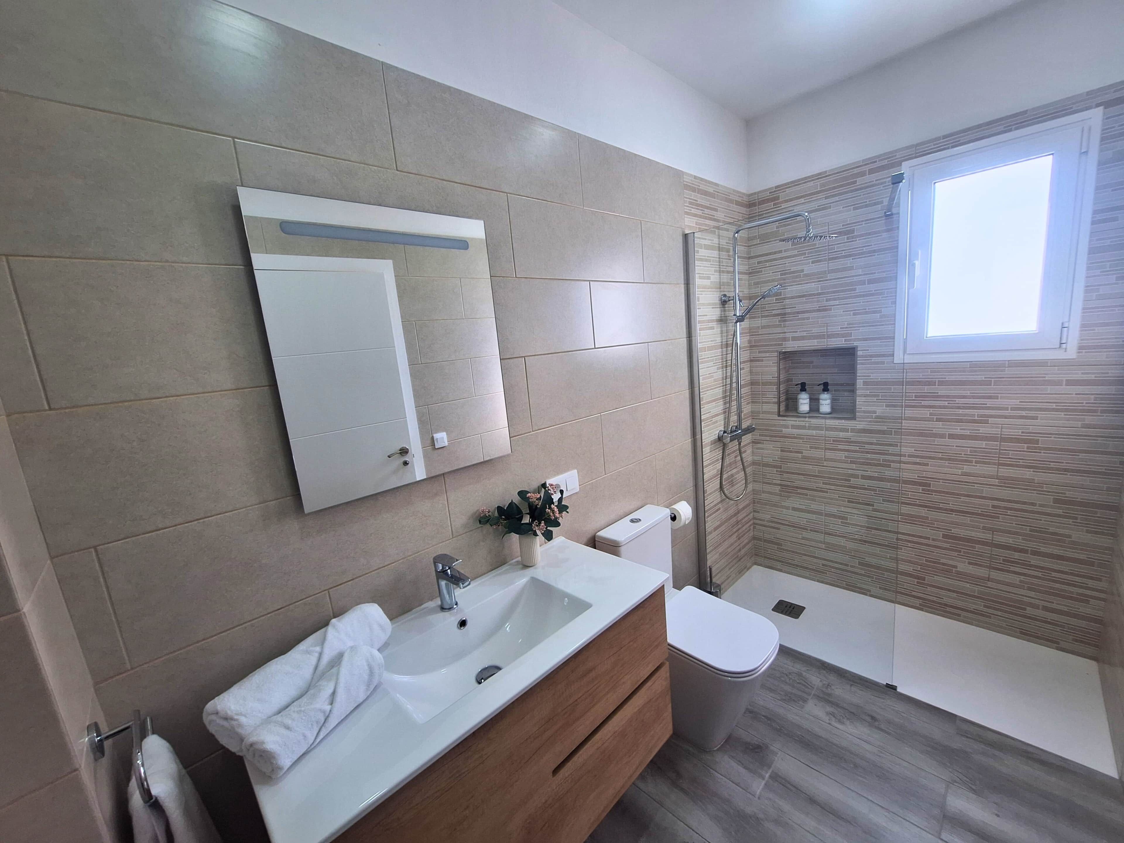 A modern bathroom with a large mirror, a sink, a toilet, and a shower area.