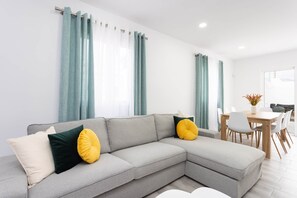 A modern living room with a grey sectional sofa, a dining table with chairs, and teal curtains. - Casa Doña Juana - Villa con jacuzzi (El Salto)