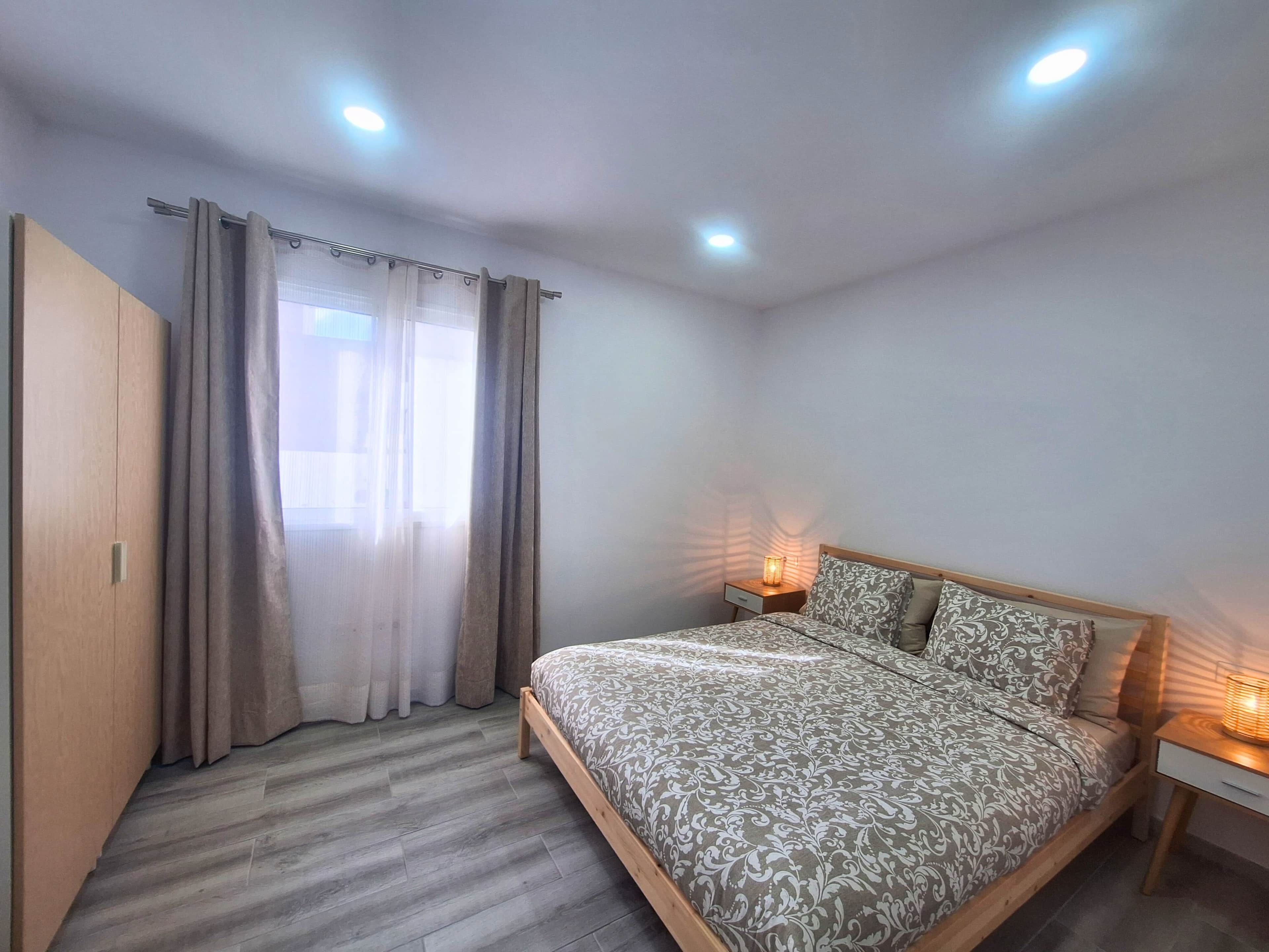 Een slaapkamer met een bed, gordijnen, een nachtkastje en een bedlampje.