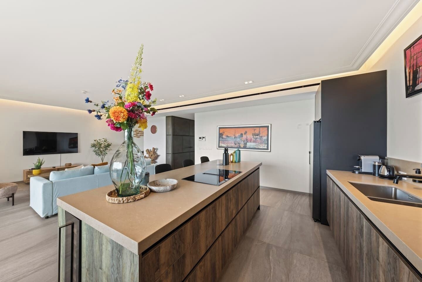 A modern kitchen with a central island, a dining area with a sofa, and a flat-screen TV mounted on the wall.