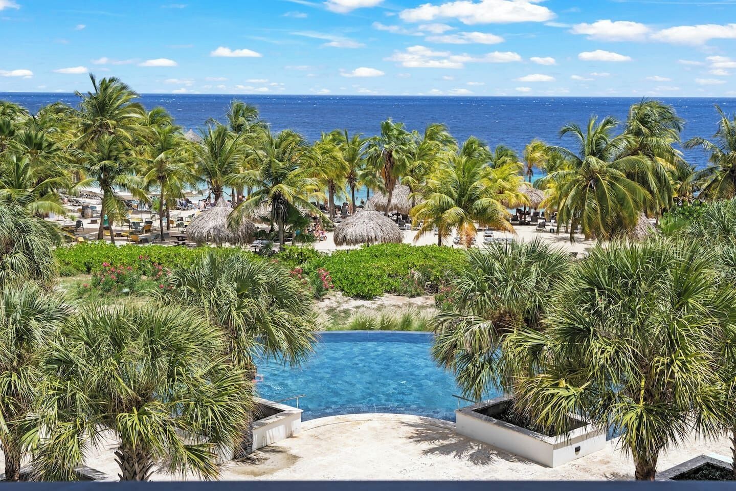 A resort with a swimming pool, palm trees, and a beach area.