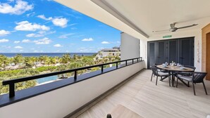Ein Balkon mit Blick auf einen Strand und das Meer, ein Esstisch mit Stühlen und ein Deckenventilator.