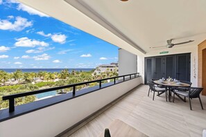 Un balcón con vista a una playa y al océano, una mesa de comedor con sillas y un ventilador de techo.