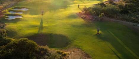 A golf course with sand bunkers, a putting green, and a flagstick.