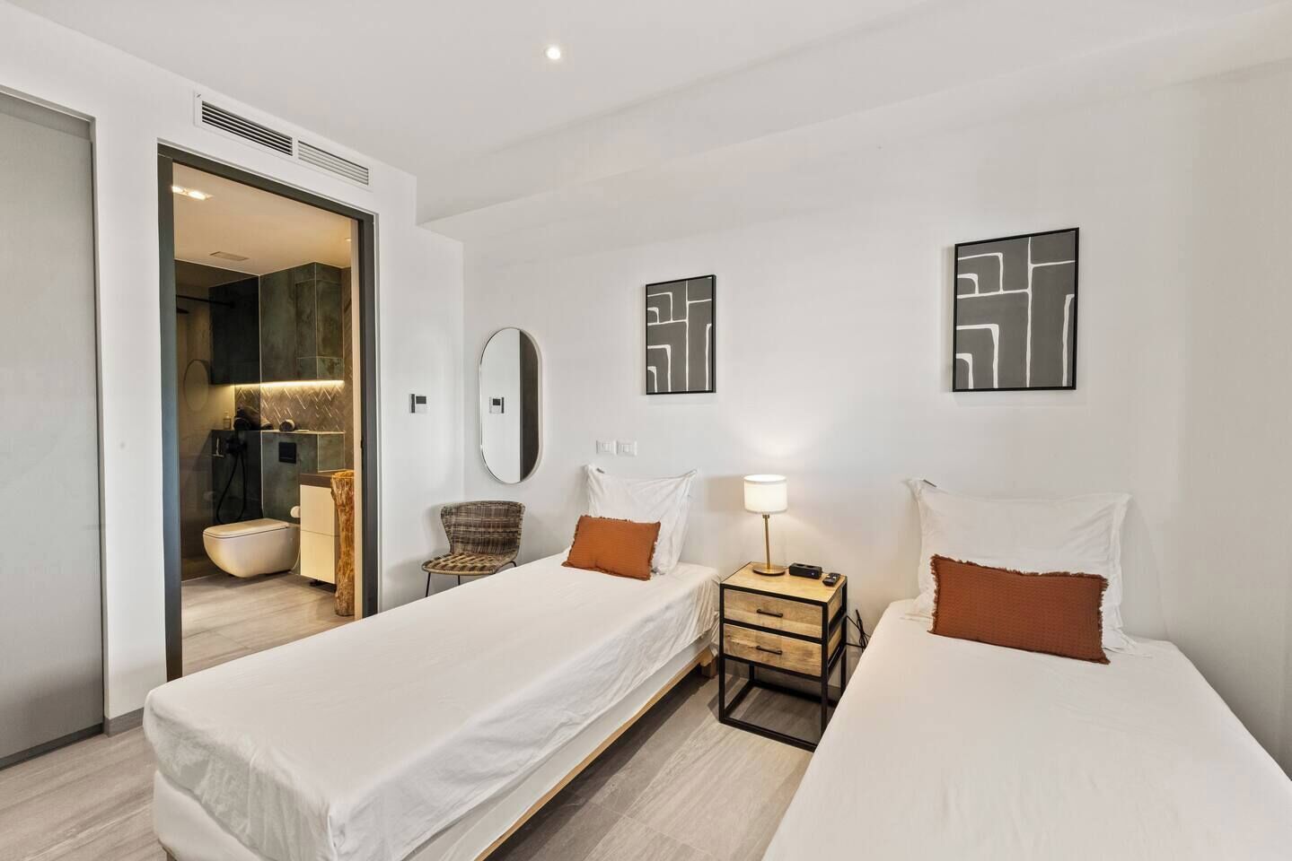 Ein Hotelzimmer mit zwei Betten, einem Sessel, einem Nachttisch mit Lampe und einem Spiegel an der Wand.