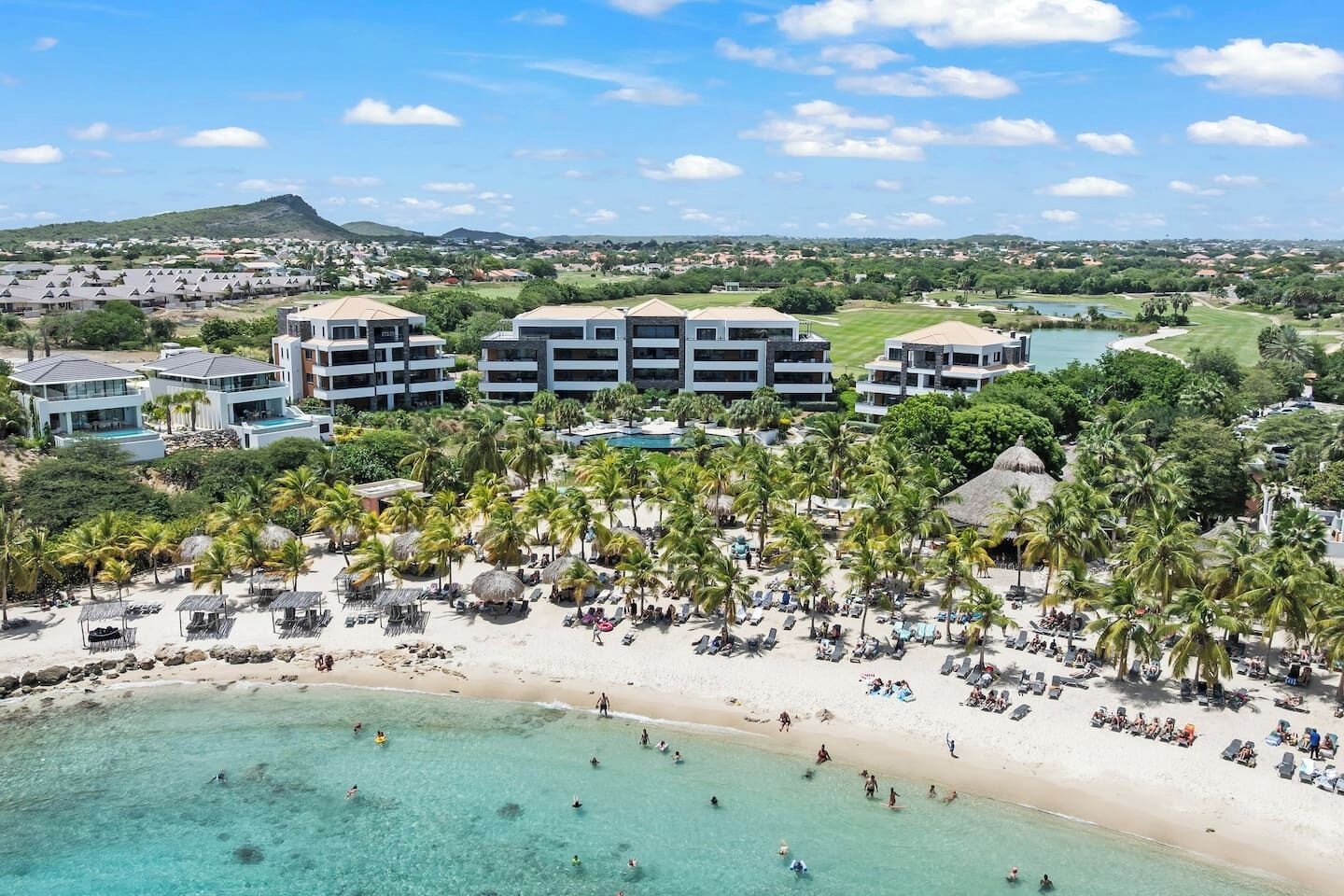 Een resort met accommodaties direct aan het strand, een zwembad en een strand met palmbomen.