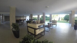 A spacious indoor area with a sofa, chairs, and a dining table. There are potted plants and a view of greenery outside.