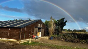 Ein hölzernes Bauernhaus mit geneigtem Dach, einer Schubkarre und einem Blumentopf im Vordergrund.