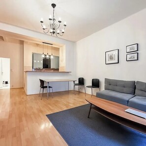 Ein modernes Wohnzimmer mit einem grauen Sofa, einem Holztisch und einem Essbereich mit Küchenzeile und Stühlen.