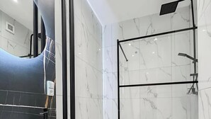 Et moderne badeværelse med en hvid marmorvask, en brusekabine med glasvægge og et sort toiletbord.
