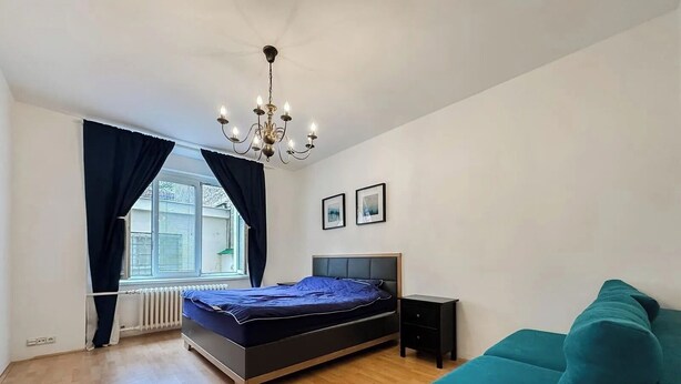 Et soveværelse med seng, kommode, stol, radiator og et vindue med gardiner.