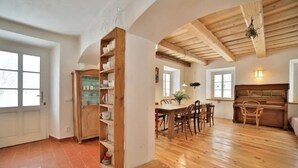 Un'ampia zona giorno con pavimento in legno, un tavolo da pranzo con sedie, un pianoforte e una libreria.