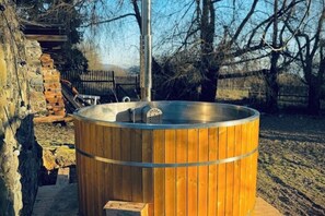 Un bain à remous en bois, doté d’une structure métallique, entouré d’un mur de pierres et d’une terrasse en bois.