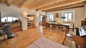 Un'ampia zona giorno con pavimento in legno, un pianoforte, un tavolo da pranzo con sedie e una cucina sullo sfondo.