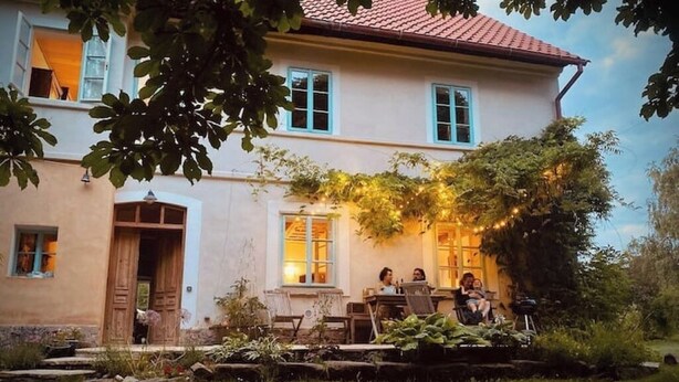 Una casa a due piani con un patio giardino, una porta in legno e un'area pranzo con persone sedute.