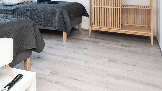 Une chambre moderne avec deux lits, une armoire en bois et une table de chevet blanche dotée d’une télécommande.
