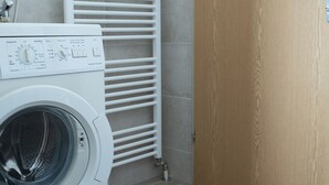 Un espace buanderie comprenant un lave-linge à chargement frontal, un porte-serviettes blanc et une porte en bois.